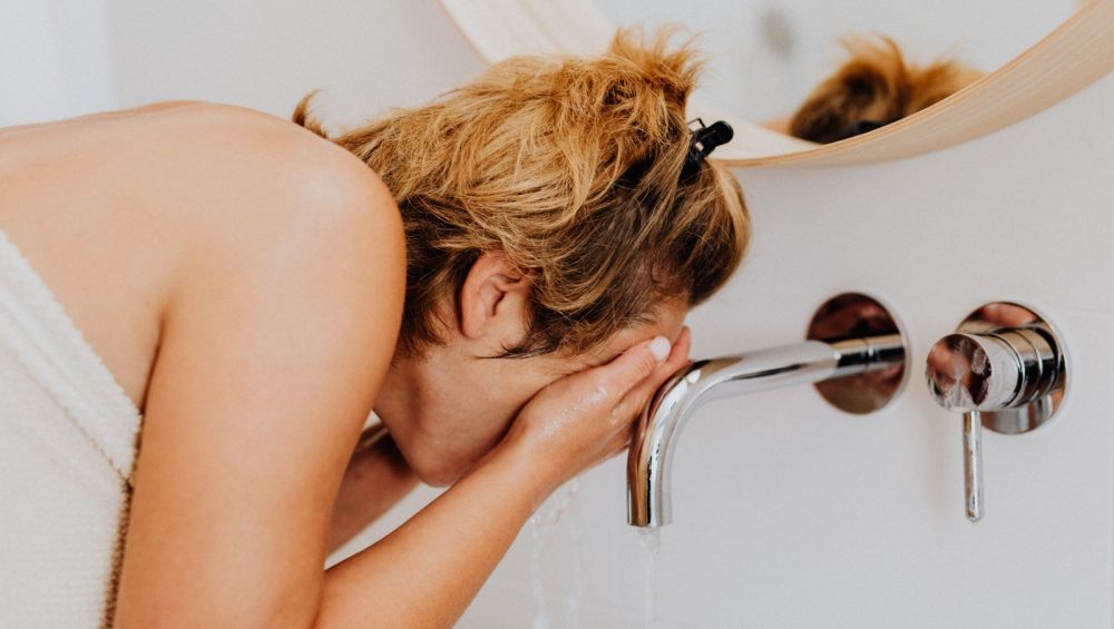 Woman washing her face at a bathroom sink