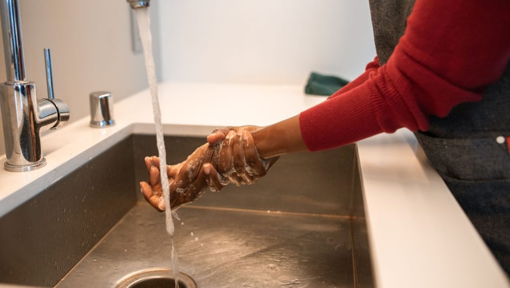 Hands being rinsed under running water at a sink