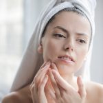 Woman with a towel wrapped in her hair looking at her skin