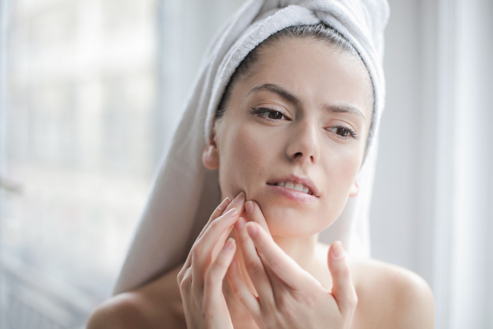 Woman with a towel wrapped in her hair looking at her skin