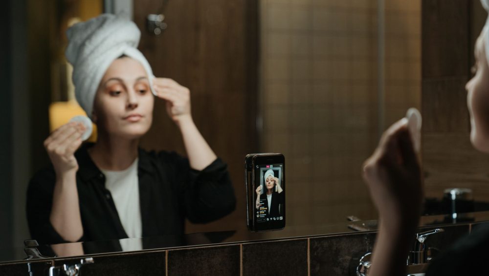 Woman in a bathroom mirror wiping her face with a cotton pad