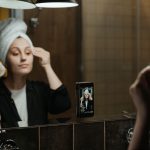 Woman in a bathroom mirror wiping her face with a cotton pad
