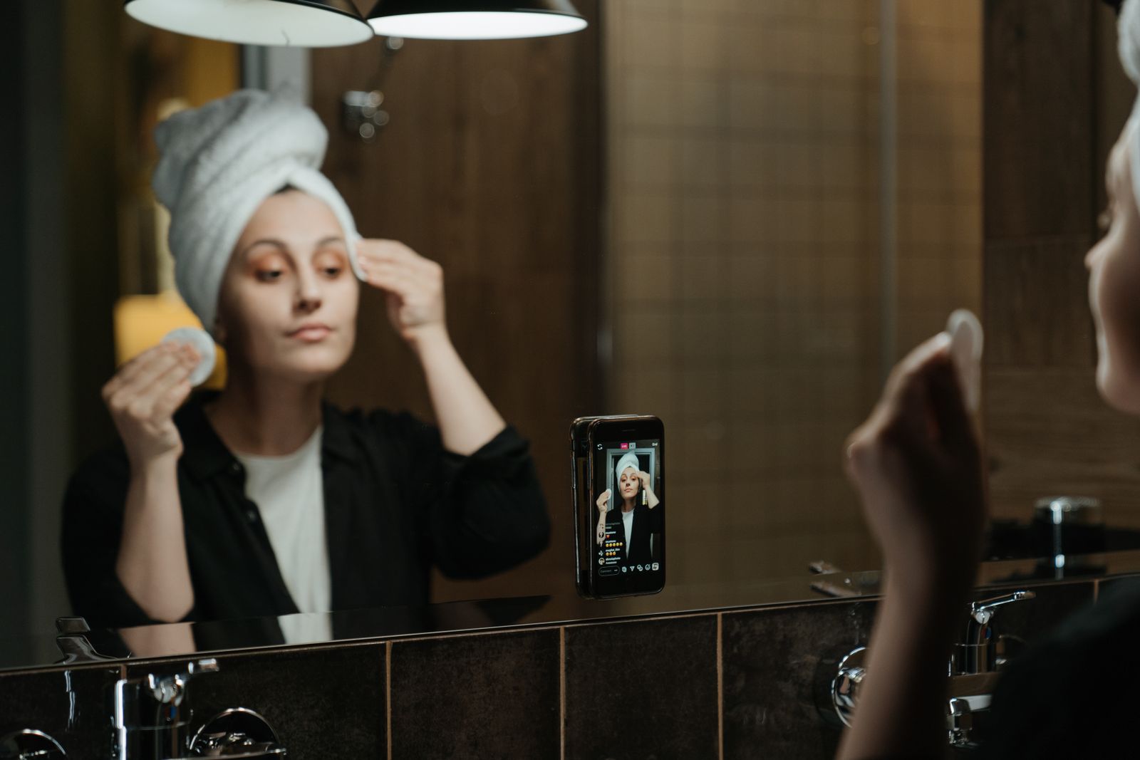 Woman in a bathroom mirror wiping her face with a cotton pad