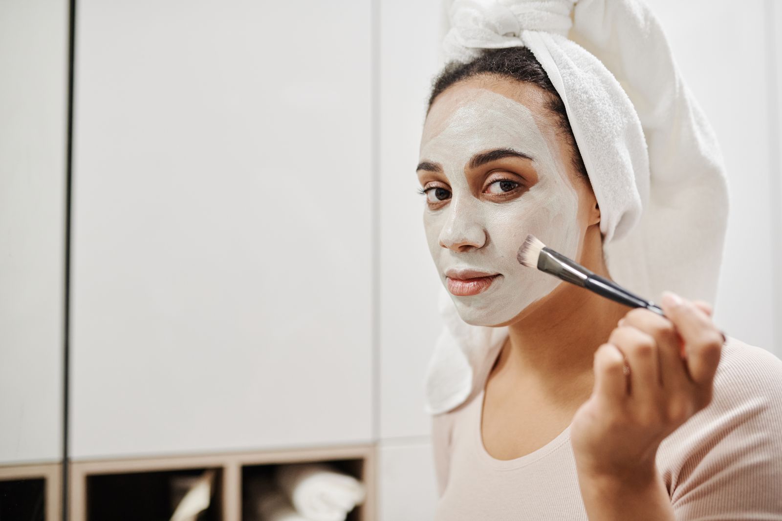 Woman applying a clay face mask with a flat brush