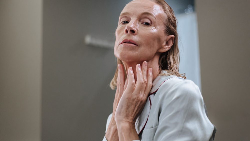 A mature woman applying skincare to her face
