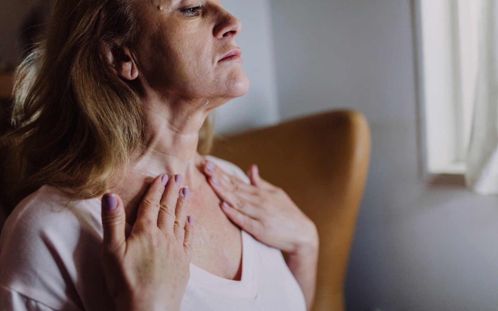 Mature woman applying skincare to her neck and decollete