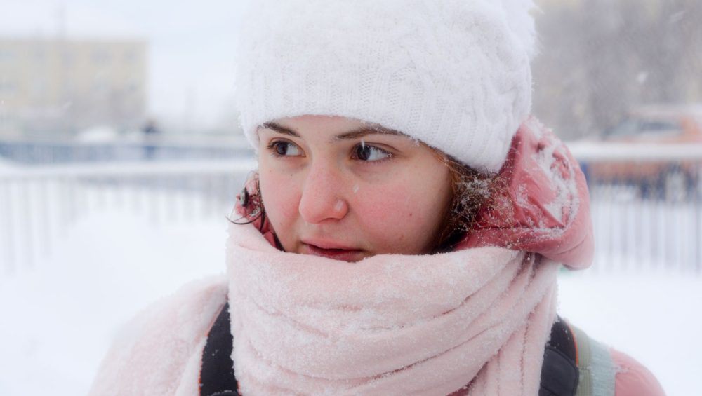Woman with flushed cheeks wrapped in a scarf outdoors in the snow