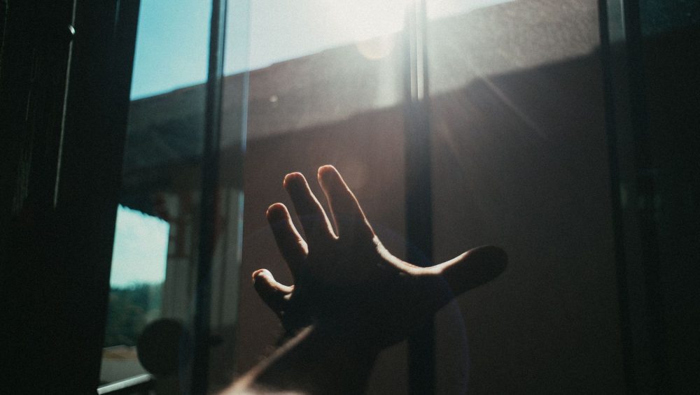 A hand reaching toward sunlight at a window