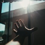 A hand reaching toward sunlight at a window