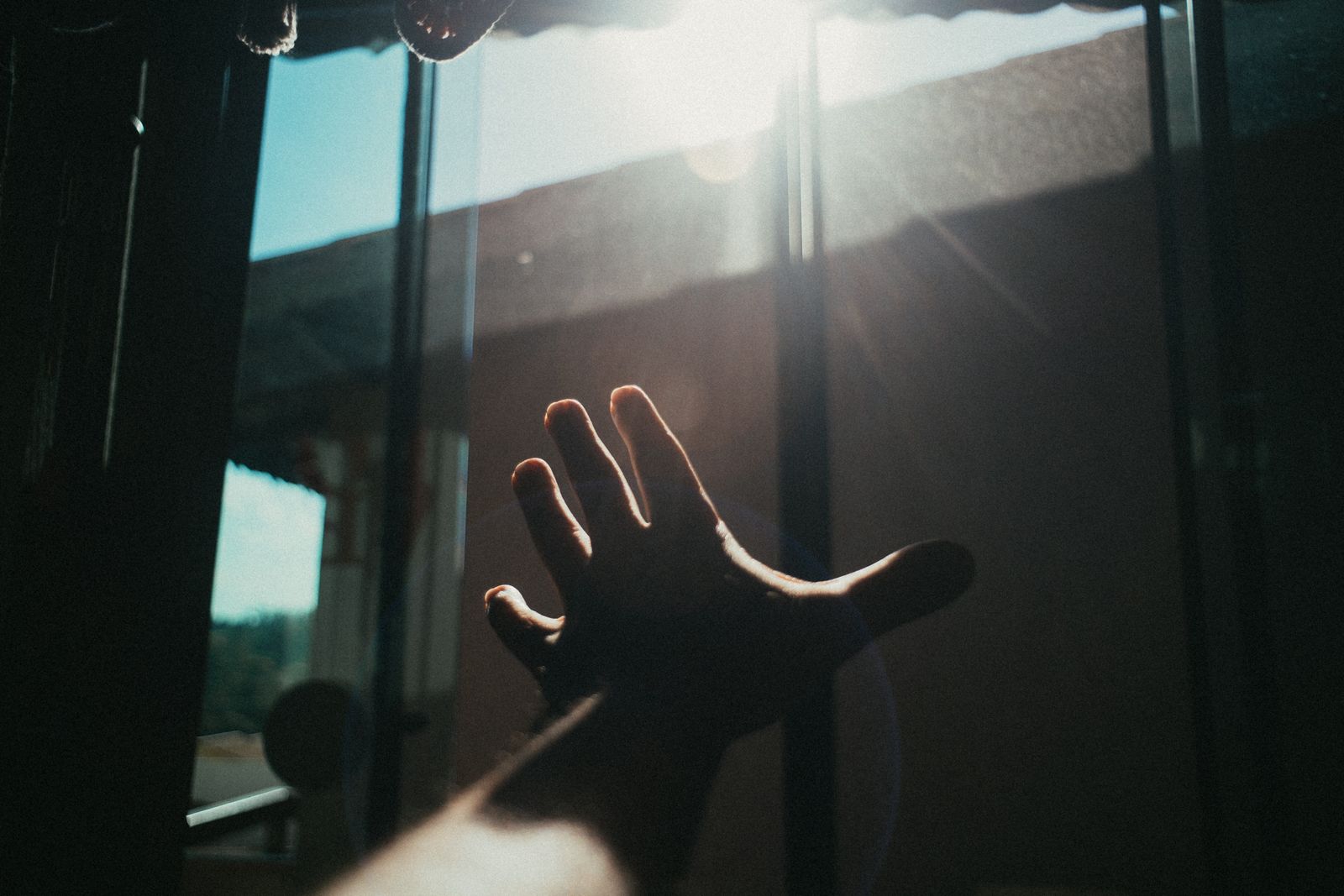 A hand reaching toward sunlight at a window