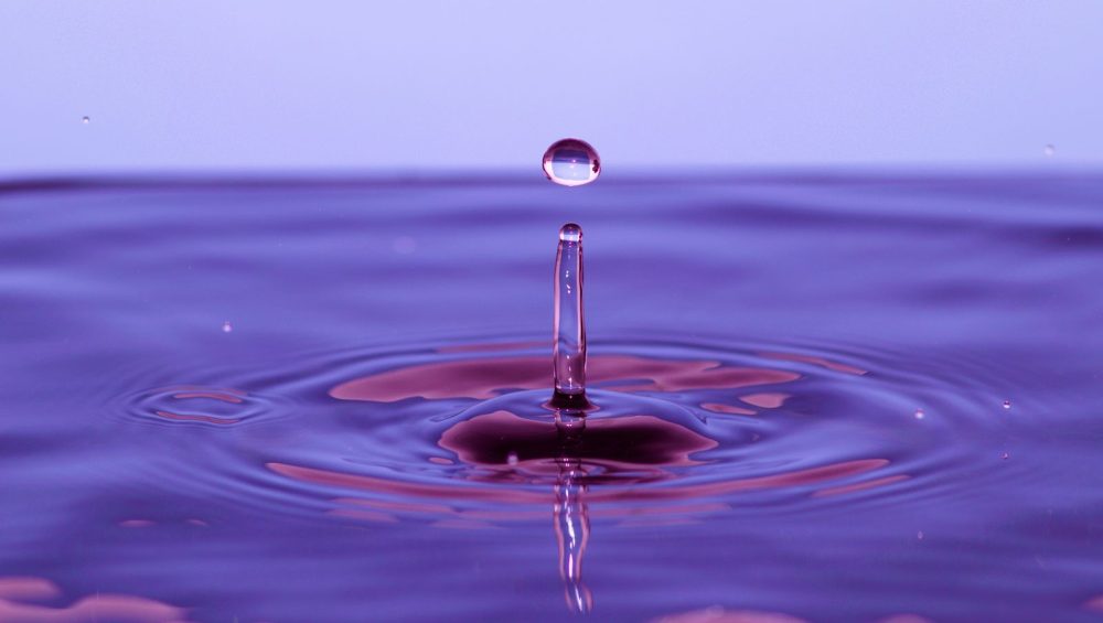 A single drop falling into violet liquid