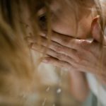A woman rinsing her face with cupped hands over a basin, water dripping from her fingers in warm light