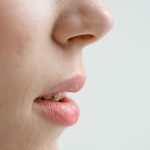 Close side view of a nose, cheek and lips against a pale background, bare skin with natural pores visible on the nose