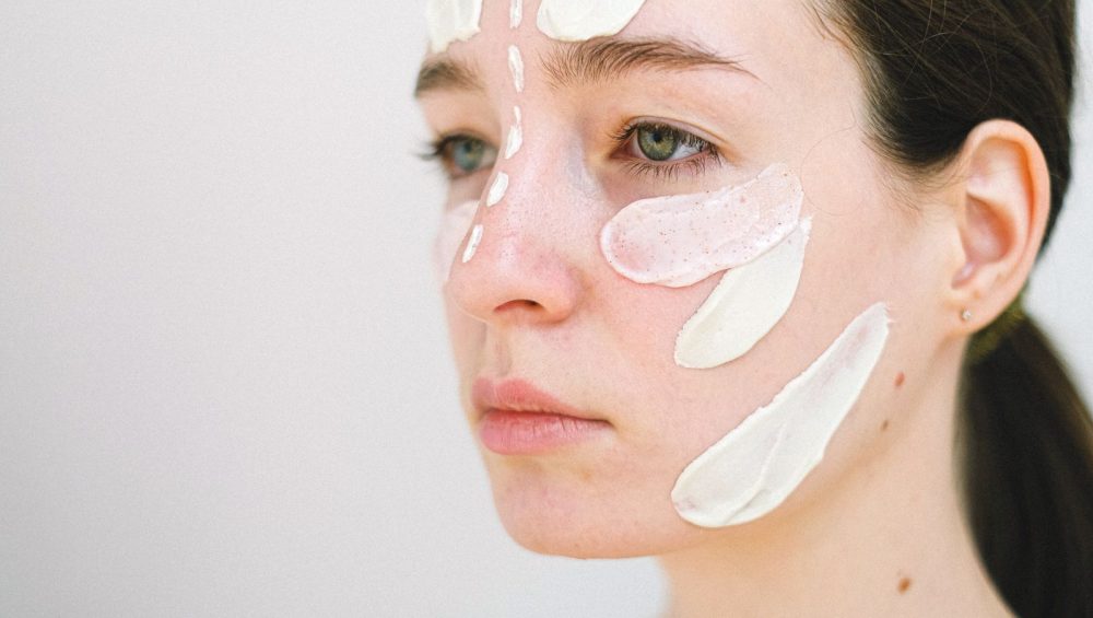 Close view of a woman's face with strokes of different textures on her cheek, nose and forehead, from a translucent gel to a thick white cream