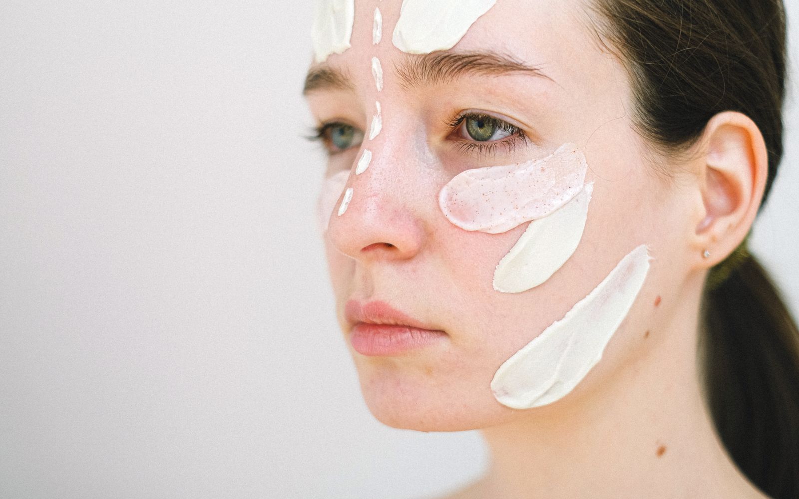 Close view of a woman's face with strokes of different textures on her cheek, nose and forehead, from a translucent gel to a thick white cream