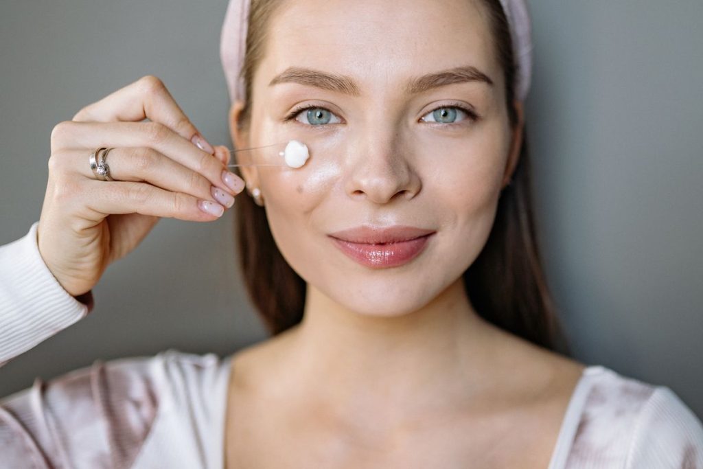 A woman dotting a small amount of moisturizer onto her cheek with one fingertip, no container in frame