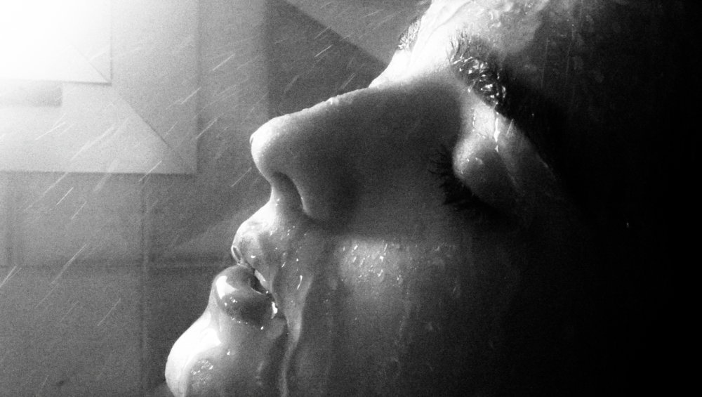 Black and white close view of a face in profile, eyes closed, under a fine spray of water