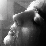 Black and white close view of a face in profile, eyes closed, under a fine spray of water
