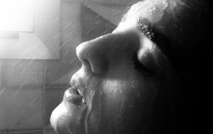 Black and white close view of a face in profile, eyes closed, under a fine spray of water