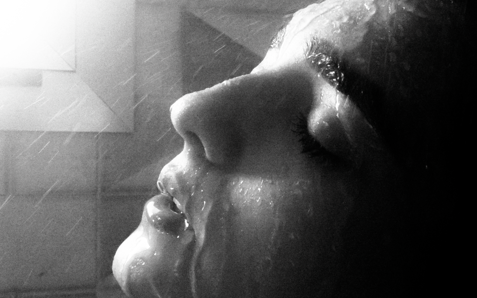 Black and white close view of a face in profile, eyes closed, under a fine spray of water
