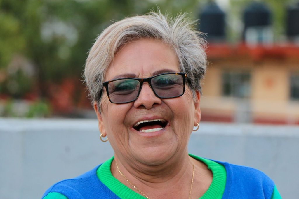 A woman in her sixties with glasses laughing outdoors, expression lines around her eyes and mouth