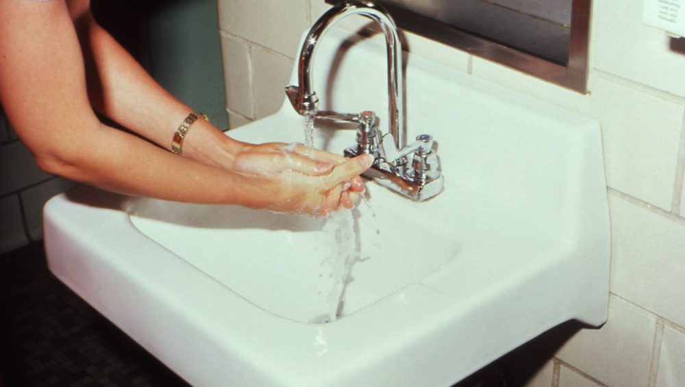 Close view of a woman's hands lathering with soap under running water at a white wall mounted sink