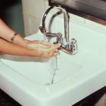 Close view of a woman's hands lathering with soap under running water at a white wall mounted sink