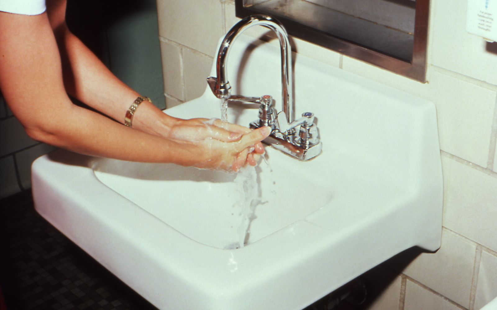 Close view of a woman's hands lathering with soap under running water at a white wall mounted sink