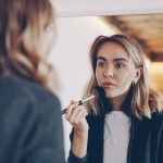A woman at a mirror at home sweeping a soft makeup brush across her cheek