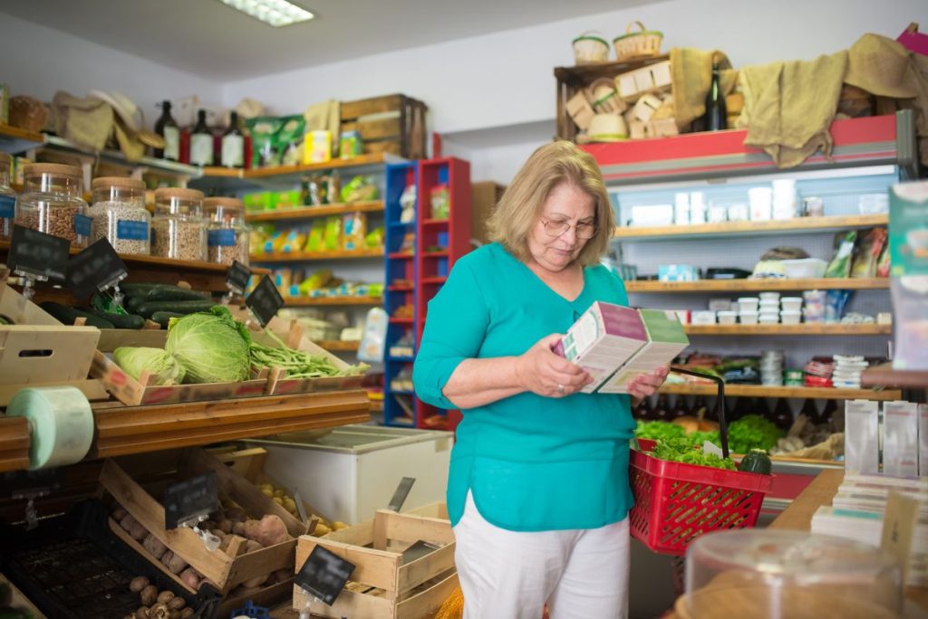 A woman in a small grocery store reading the printed label on a packaged item