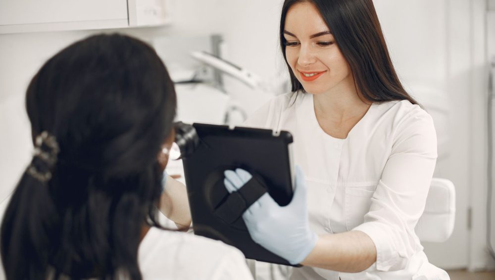 An aesthetician showing a client something on a tablet during a consultation in a bright treatment room