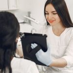 An aesthetician showing a client something on a tablet during a consultation in a bright treatment room