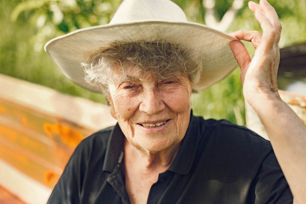 A woman in her seventies outdoors wearing a wide-brimmed sunhat, smiling