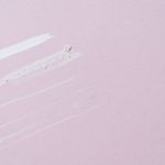 A few swatches of different textures side by side on a pale pink surface, from a thick white cream to thin, sheer strokes