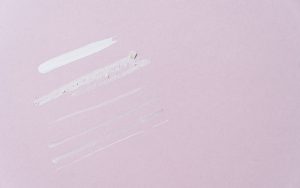 A few swatches of different textures side by side on a pale pink surface, from a thick white cream to thin, sheer strokes