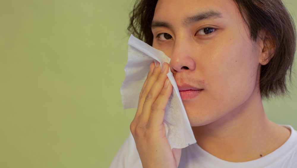 A person lightly pressing a sheet of tissue to the cheek