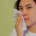 A person lightly pressing a sheet of tissue to the cheek