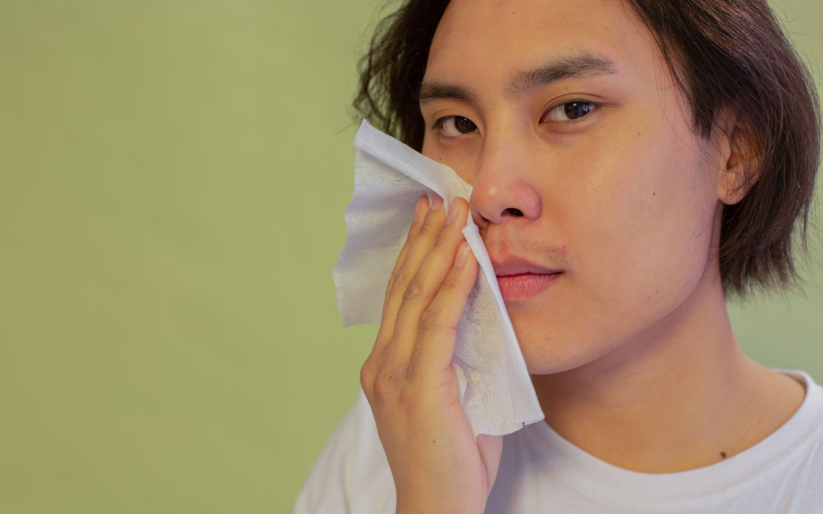 A person lightly pressing a sheet of tissue to the cheek