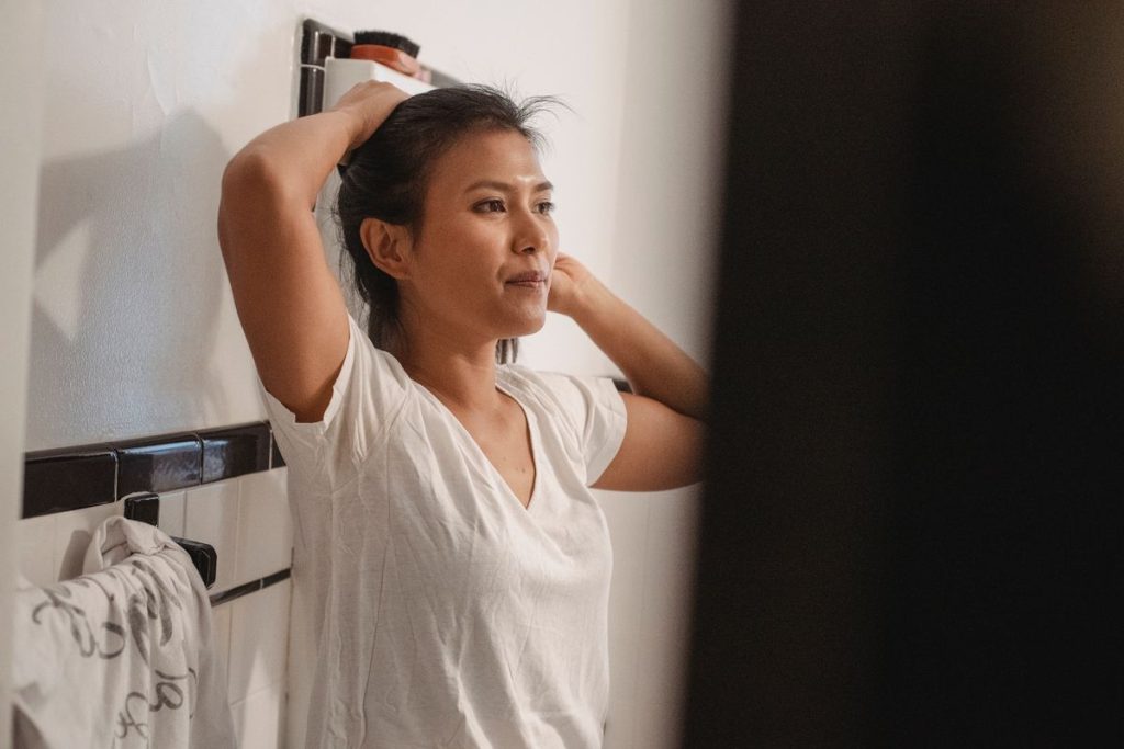 A woman tying her hair back in a bright bathroom before cleansing