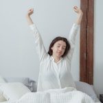 A woman stretching as she sits up in bed in early morning light