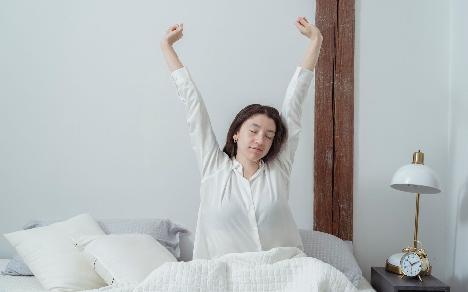 A woman stretching as she sits up in bed in early morning light
