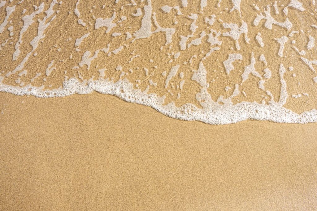 Sea foam washing over pale golden sand at the shoreline in bright daylight