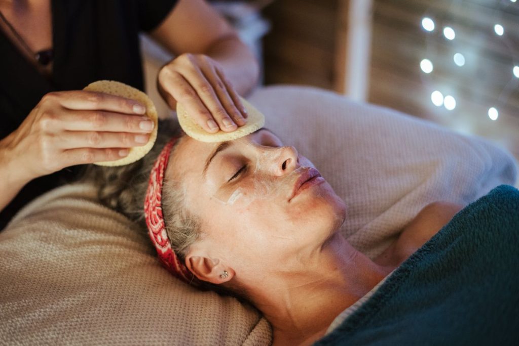 A practitioner gently pressing two soft facial sponges to the forehead of a woman lying back with her eyes closed