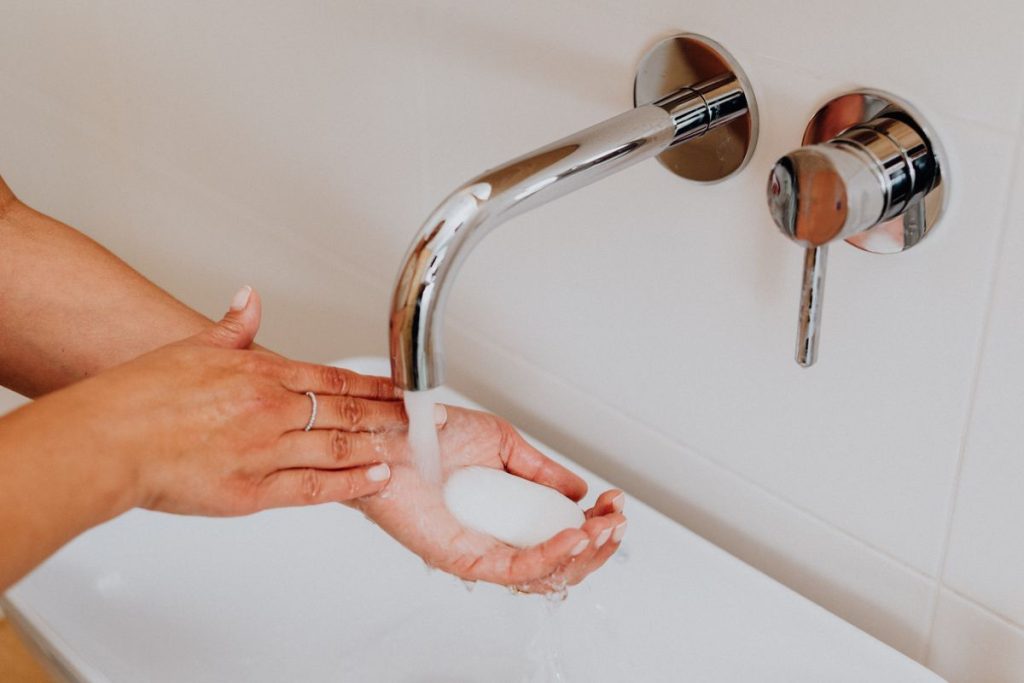 Hands rinsing under a wall-mounted tap over a white basin