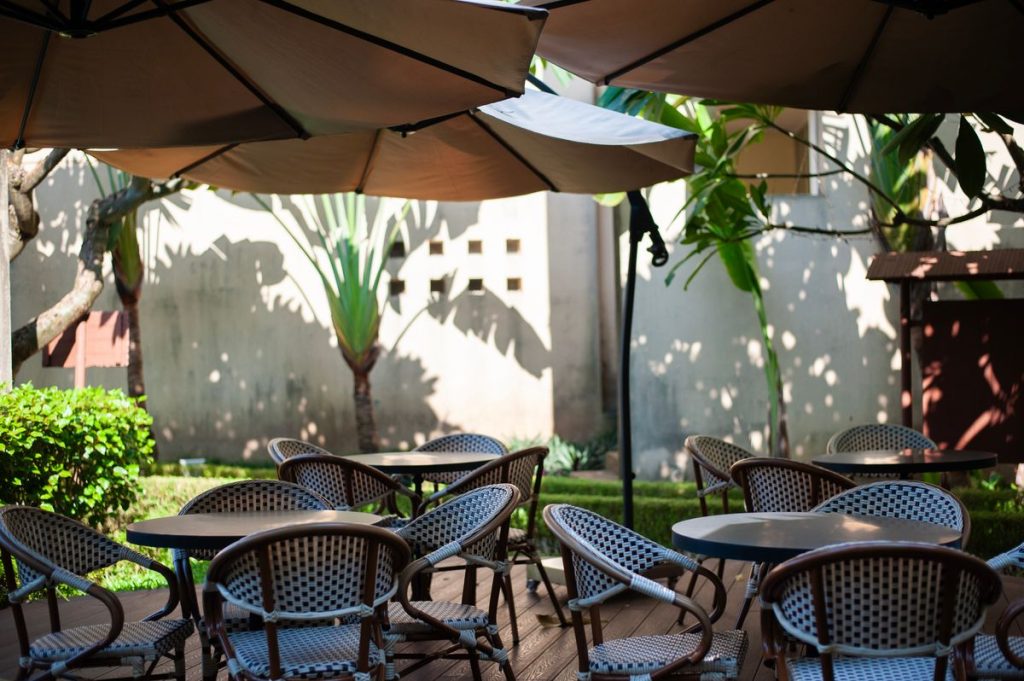 Outdoor café tables and chairs under large umbrellas, bright sun beyond the shade