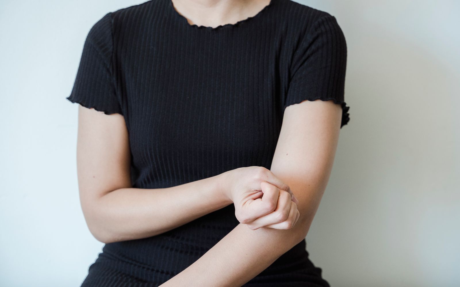 A woman in a dark T-shirt holding her forearm against a plain light background