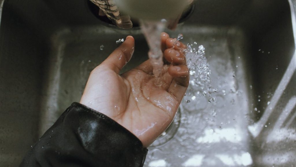 A cupped hand held under water running from a tap into a steel sink