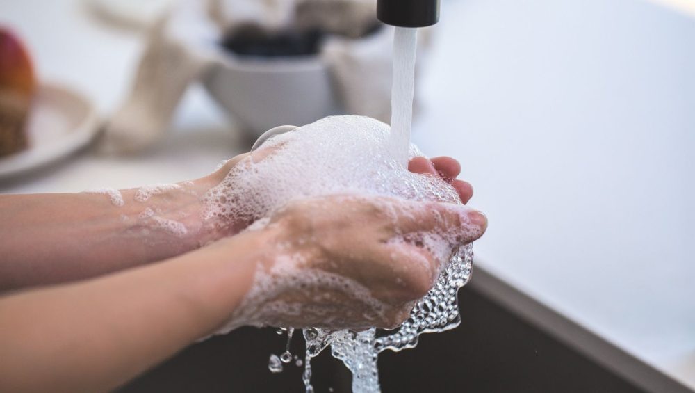 Soapy hands being rinsed under a running tap