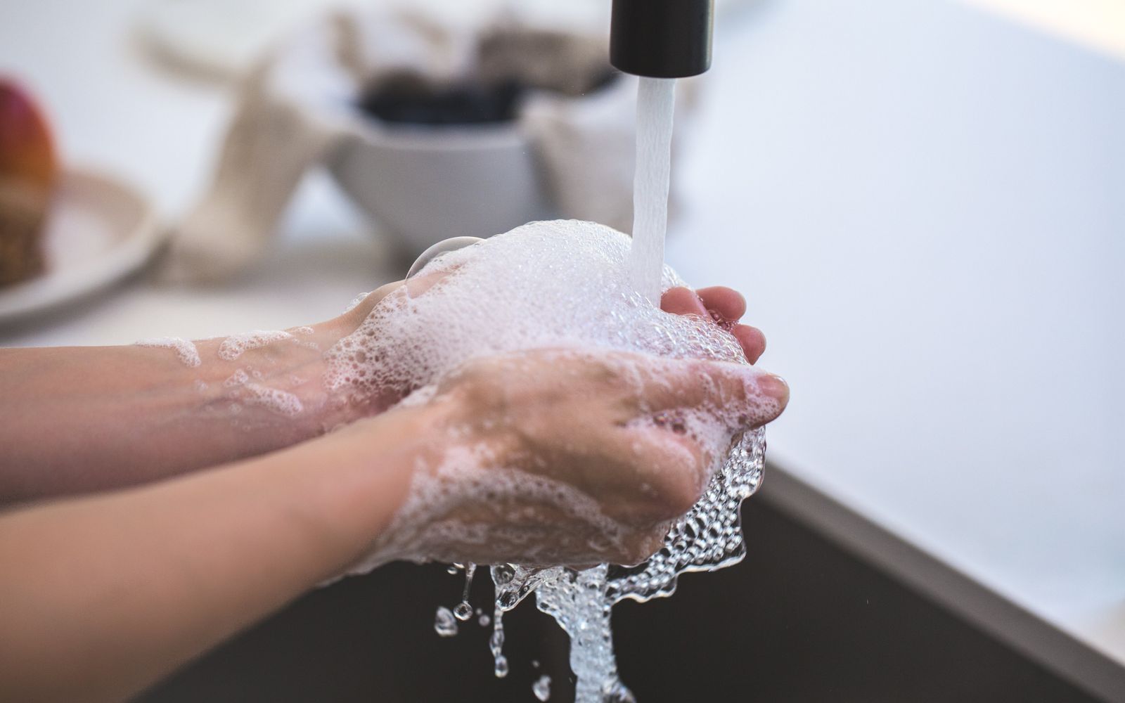 Soapy hands being rinsed under a running tap